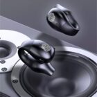 Close-up of two black wireless earbuds with fingerprint design, floating above a circular speaker. The earbuds have a sleek, modern design, showcasing advanced technology. The background is metallic with the speakers surface visible.