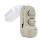 A beige hearing aid with two buttons and a transparent ear hook. The device has a textured surface and a small charging port on the side.