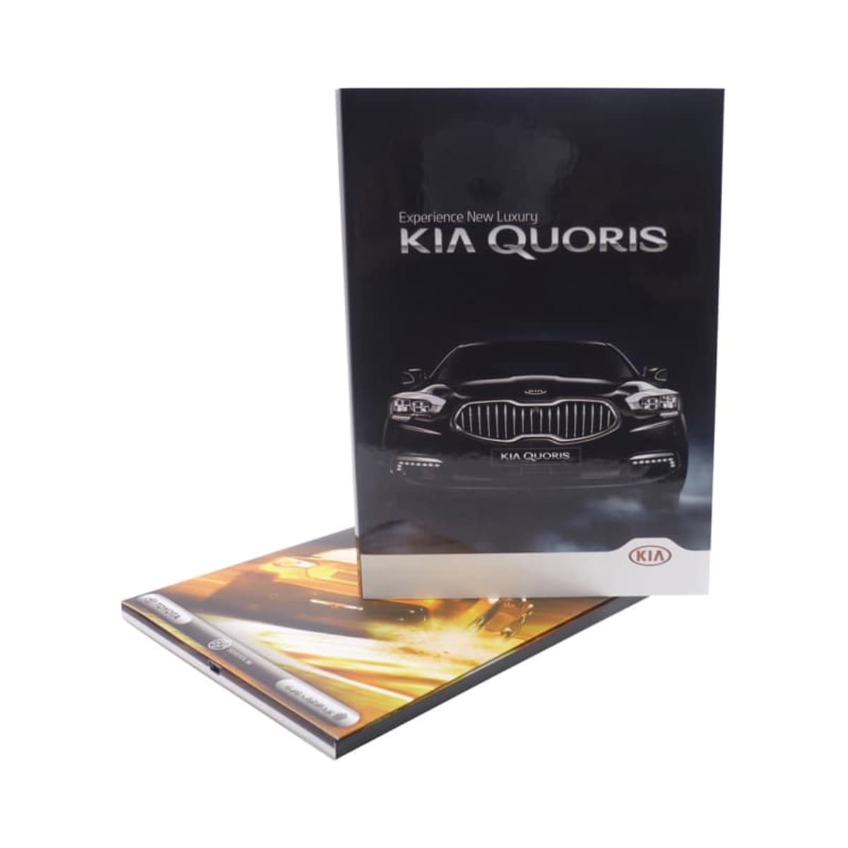 Two Kia Quoris brochures, one standing upright showing a front view of a black car with the text Experience New Luxury KIA QUORIS and the other lying flat, partially visible with a blurred image of a car in motion.