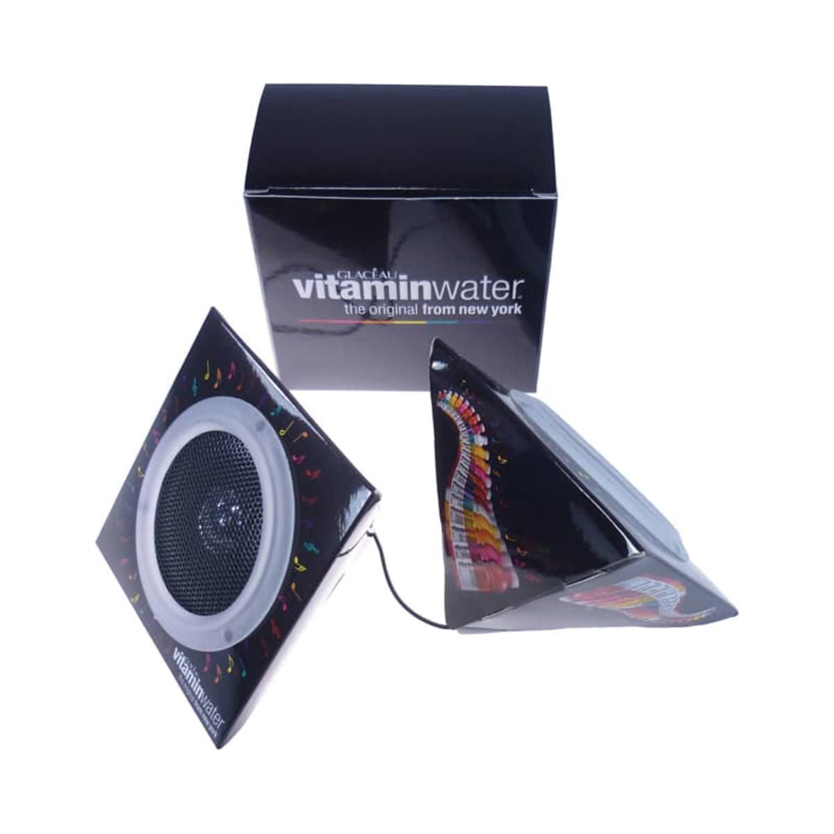Two black pyramid-shaped speakers with a colorful design on the sides are connected by a cord. Behind them is a black box labeled vitaminwater, the original from new york with white text.