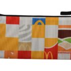 A colorful McDonalds-themed zippered pouch with a pixelated design featuring abstract patterns and elements like burger layers and the McDonalds logo. A loop handle is attached to the side.