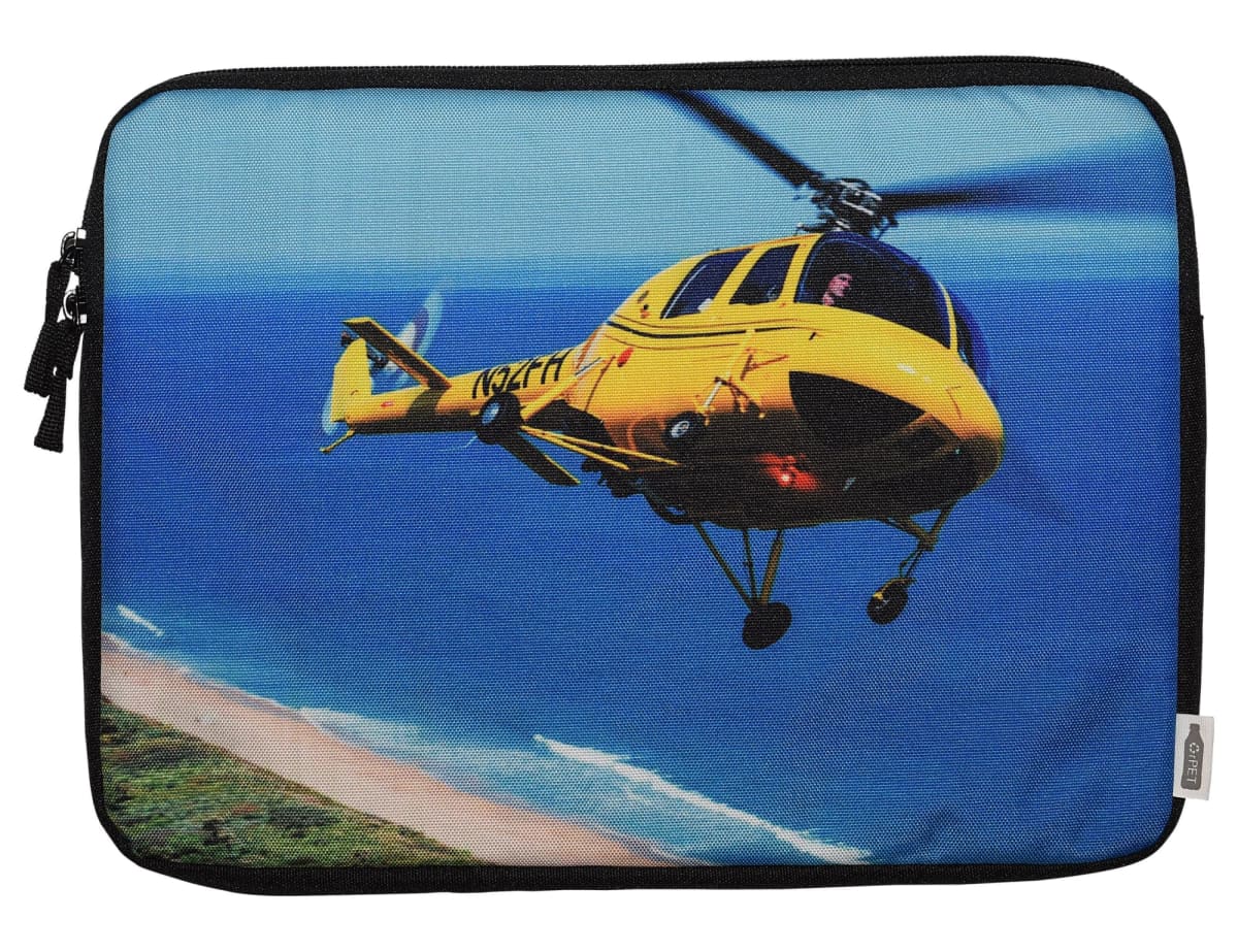 A yellow helicopter flies over a coastal landscape with a sandy beach and blue ocean. The image is printed on a fabric case with a zipper on the side.