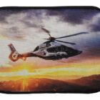 A helicopter flies against a dramatic sunset sky, with vibrant orange and purple hues. Mountains are silhouetted at the horizon, highlighting the helicopters sleek design and dynamic movement.