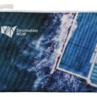 A zippered pouch featuring an aerial view of ocean waves crashing against a pool. The text Destination NSW is visible on the upper left corner of the pouch.