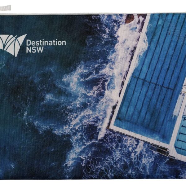 Aerial view of an ocean pool with waves crashing over the edge. The image includes the text Destination NSW. The pool contrasts with the deep blue of the ocean, creating a dynamic scene.