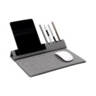 A sleek desk organizer holds a tablet, four pens, and a wireless charging pad. A computer mouse sits on the gray fabric surface, combining functionality with a minimalist design.