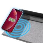 A smartphone with a charging symbol hovers above a gray fabric wireless charging pad emitting blue waves, indicating active charging.