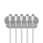 A cable organizer holding five white USB cables neatly in place. The organizer is made of two overlapping fabric bands in shades of gray, attached to a wall or surface.