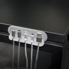 A cable organizer attached to the edge of a dark desk holds five different types of charging cables, arranged in a row for easy access. The cords are neatly secured in the organizer slots.