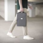 Person walking in an empty parking garage, holding a gray laptop bag in their left hand. Theyre wearing beige pants, a dark green shirt, and white sneakers. The focus is on the bag, while the background is blurred.