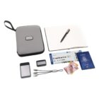 A travel kit featuring a grey zippered case, an open notebook with a pen, a boarding pass, a passport, currency notes, a smartphone, a power bank, and a charging cable.