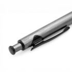 Close-up of a metallic pen with a textured finish. The pen features a push-button mechanism at the top and a black clip attached to its side. The tip is not visible. The background is plain white.