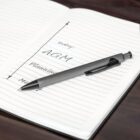 A pen rests on an open notebook. The page lists items: AGM under Todays and Planning & Meeting beneath it. Lines draw a timeline connecting the items, suggesting a schedule or agenda for the day.