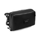 A sleek black crossbody bag with a minimalist design, featuring a strap and a small rectangular logo patch on the front that reads House of Revolutions. The bag appears to have a smooth texture with a front zippered pocket.