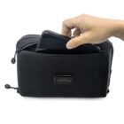 A hand places a smartphone into a black toiletry bag with the label House of Revolutions. The bag has a zipper and is set against a plain white background.