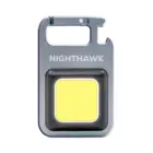Meet the Nighthawk Compact LED Tool—a small, square-shaped carabiner light with NIGHTHAWK printed on its metallic finish. It features a large yellow light panel at the center, ideal for illuminating your adventures.