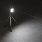 A small, bright LED light mounted on a tripod, illuminating a dark, tiled floor. The light creates a focused beam, highlighting the texture of the tiles in contrast to the surrounding shadow.