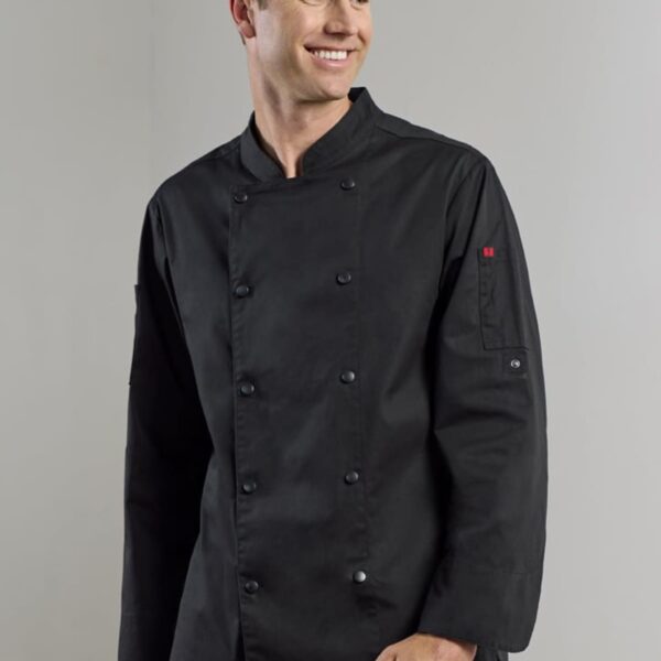 A person wearing a black double-breasted chef jacket smiles while standing. The jacket has long sleeves and button details on the cuffs and front, set against a plain, light gray background.