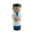 Toy figure of a smiling doctor wearing a white lab coat, blue tie, and dark pants. The figure holds a clipboard and a pen.