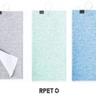 Three towels are displayed side by side. The towels are in shades of gray, mint green, and blue. Each towel has a loop at the top and a small black tag. The towel on the left is partially folded to show the white underside.