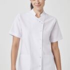 A person wearing a white short-sleeved medical or chef coat with buttons and two pockets. The background is plain and light-colored.