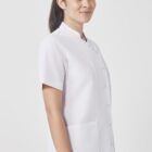 A woman with long dark hair, tied back, wears a white button-up uniform with short sleeves and a high collar. She faces the camera with a slight smile. The background is plain white.