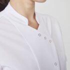 Close-up of a person wearing a white chefs jacket with a mandarin collar and button details. The background is plain and light-colored.