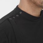 Close-up of a person wearing a black shirt with metal grommet details on the shoulder. The image focuses on the upper part of the shirt and the persons jawline, with a neutral white background.