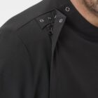 Close-up of a person wearing a black shirt with a unique design featuring metal snaps and a zipper on the shoulder, partially covering the neck. The person’s chin and part of their mouth are visible on the right side of the image.