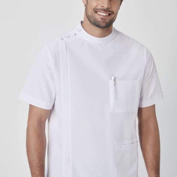 A man wearing a short-sleeved white medical uniform with button details on the shoulder and front pockets. He is smiling and standing against a plain white background.