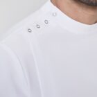 Close-up of a mans shoulder wearing a white shirt with a high collar. The shirt features three metal snap buttons on the shoulder for closure. The background is a neutral gray, highlighting the simplicity and elegance of the garment.