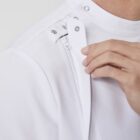 A person adjusts the high collar of a white garment, displaying the snap buttons and a partially open zipper on the shoulder.