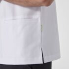 A person wearing a white short-sleeved medical scrub top with pockets, and black pants. The focus is on the side view of the torso and arm, highlighting the pocket and a small side slit at the hem.