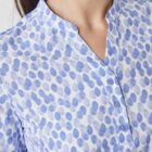 A person wearing a blouse with a blue and white spotted pattern. The blouse has a short stand-up collar and a buttoned front. The image focuses on the upper body, showing the print and style of the blouse.