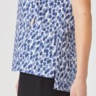 Person wearing a blue and white patterned top with a front pocket holding a pen, and black pants. The top features a design of irregular blue spots.