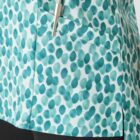 Close-up of a shirt with a turquoise and white abstract dot pattern. A pen is clipped to a pocket on the shirt. The lower part of the image shows black pants.