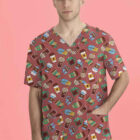 A person stands against a pink background wearing a scrub top with a playful pattern featuring various drinks and snacks. The top has a v-neck and short sleeves. The person has short hair and is looking directly at the camera.
