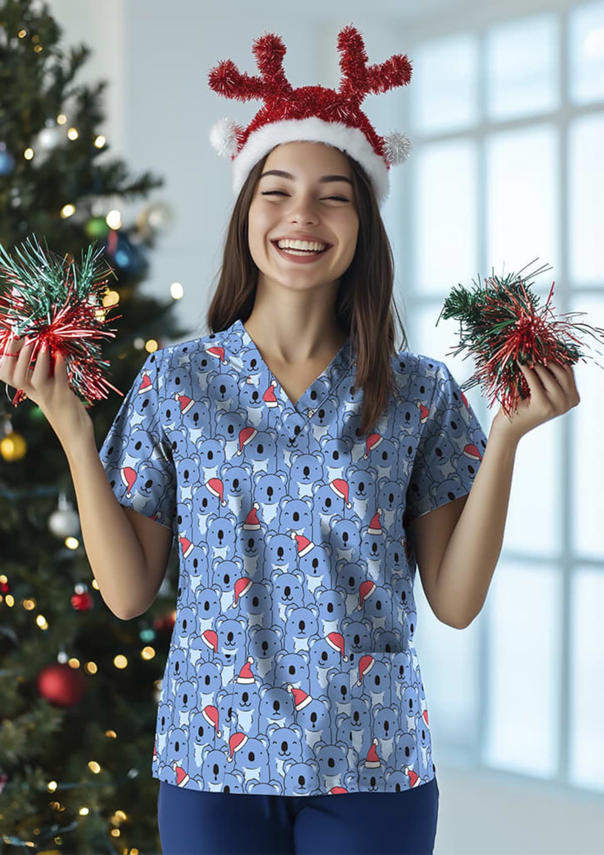 A woman wearing a festive hat and a blue shirt with a pattern of Santa hats is smiling cheerfully. She holds red and green tinsel in each hand. A decorated Christmas tree is in the background near a large window.