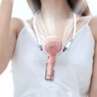 A person wearing a white tank top is using a pink portable fan hanging around their neck. The fan is blowing air upwards, with visible airflow lines. The background is blurred and bright.