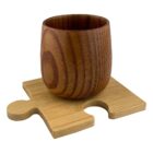 A wooden cup with distinct grain patterns sits on a square puzzle piece-shaped coaster, also made of wood. The coaster features a light wood tone with a puzzle piece cut-out on one side.
