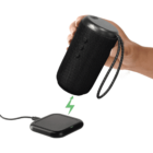 Hand holding a black portable speaker above a wireless charging pad with a green lightning bolt.