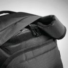 Close-up of a black backpack, showing its textured fabric with a hexagonal pattern. The image highlights the zipper and part of the padded strap, with a simple, modern design suitable for travel or daily use.