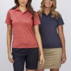 Two women smiling, both wearing casual polo shirts and shorts. The woman on the left is in a red shirt with dark shorts, and the woman on the right is in a navy shirt with a beige skirt. They stand against a plain, light gray background.