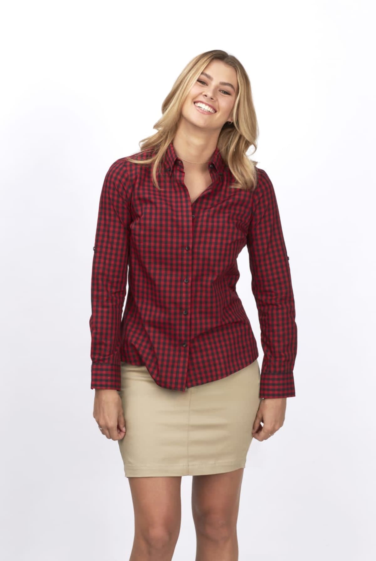 A person with long blonde hair is smiling while wearing a red and black checkered shirt and a beige skirt. The white background adds to the focus on the outfit.