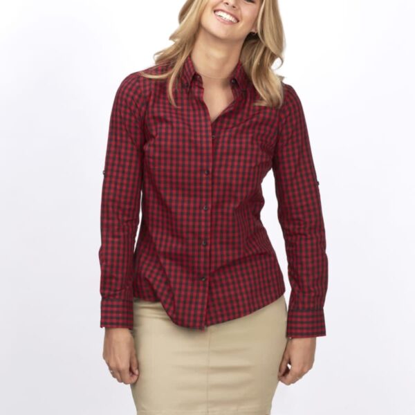 Woman smiling, wearing a red and black checkered shirt and a beige skirt, standing against a plain white background.