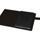 Open black notebook with 275 Kent embossed on the cover, placed on a desk with a black cover flap partially open to the left.