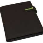 A black leather planner with a flap closure. The word Herbalife is printed in green on the flap, which features a small leaf design.
