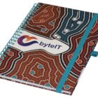 A spiral-bound notebook with a colorful dot pattern cover and a blue elastic band. The cover features the text byteIT with a logo.