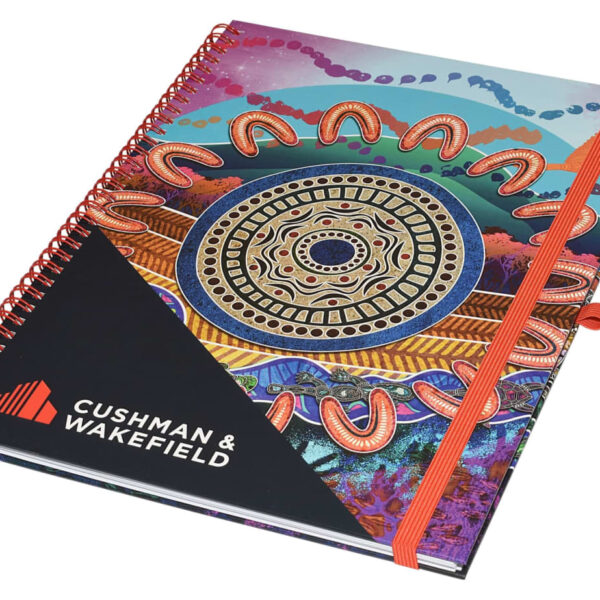 A colorful spiral-bound notebook with an intricate, abstract design featuring circular and wave patterns. The cover displays the Cushman & Wakefield logo in the bottom left corner. The notebook is secured with an orange elastic band.