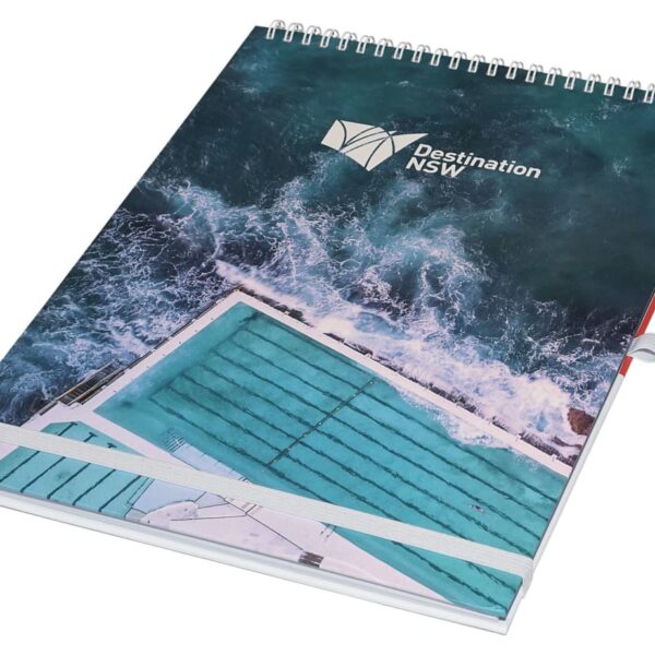A spiral-bound notebook with a cover showing an aerial view of an ocean pool by the sea. The words Destination NSW are printed on the cover.
